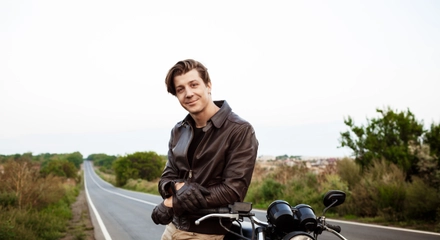 Young handsome man posing near his motorbike countryside road