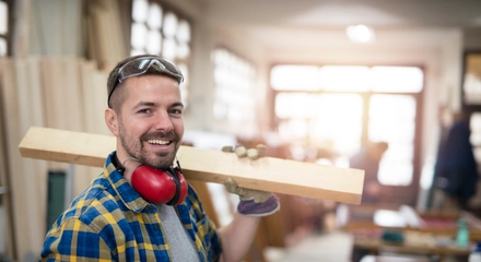 Portrait professional carpenter holding wood plank material his shoulder smiling
