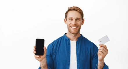Smiling happy man showing mobile phone blank screen bank credit card recommending smartphone application online shopping app standing white background